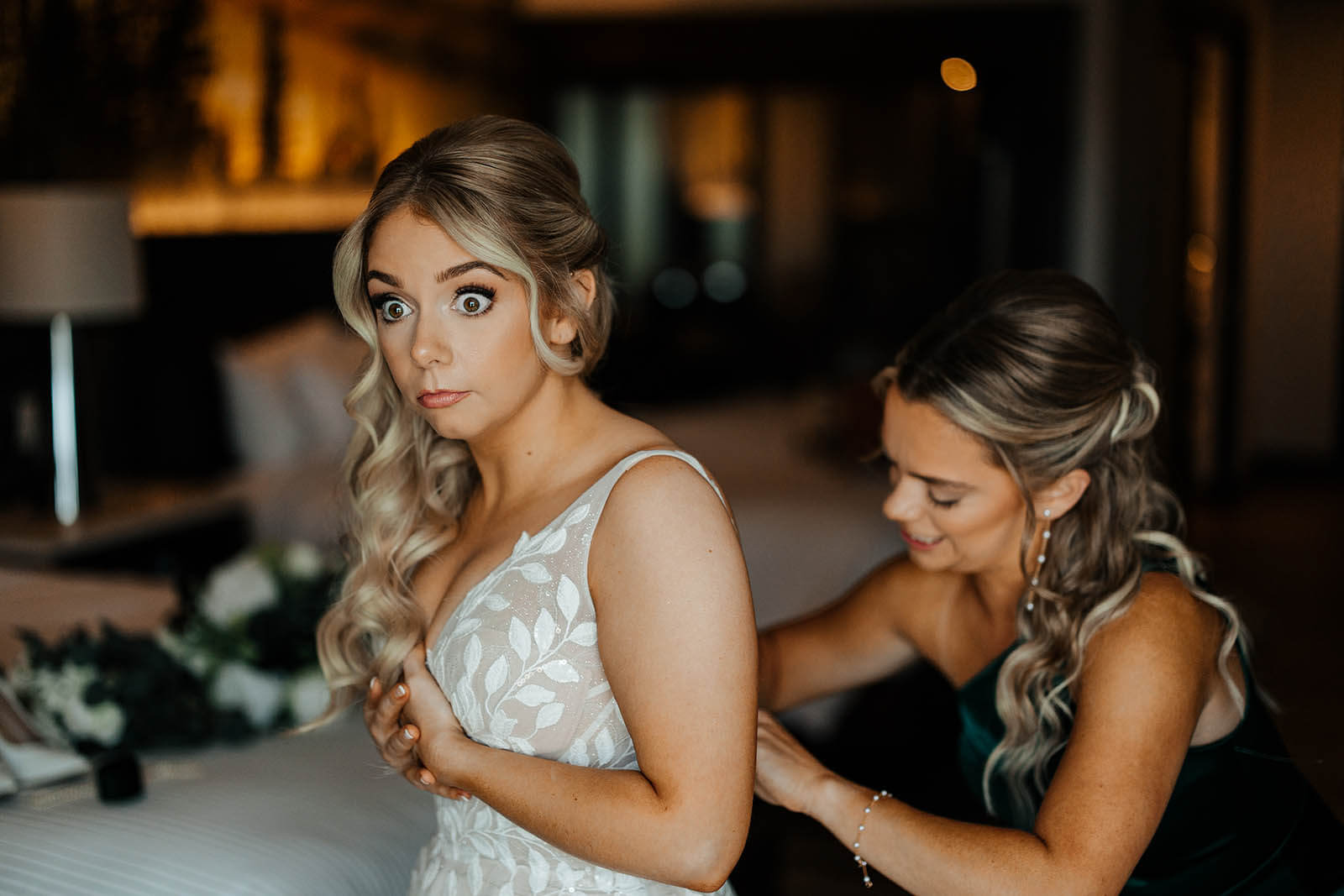 GAUPERphoto Detroit Michigan wedding photographer Packard Proving Ground candid bride wide-eyed reaction while bridesmaid buttons wedding gown getting ready, top documentary Michigan wedding photography