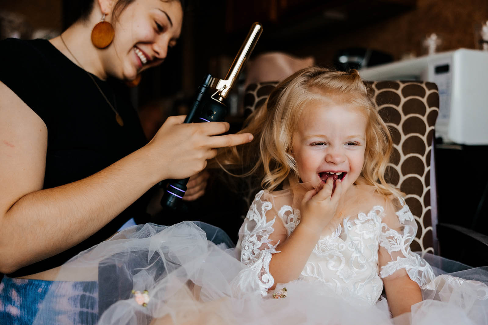 Shoreline Inn wedding photographer Muskegon Michigan candid flower girl laughing with delight while getting hair curled during wedding morning getting ready, best West Michigan documentary wedding photography