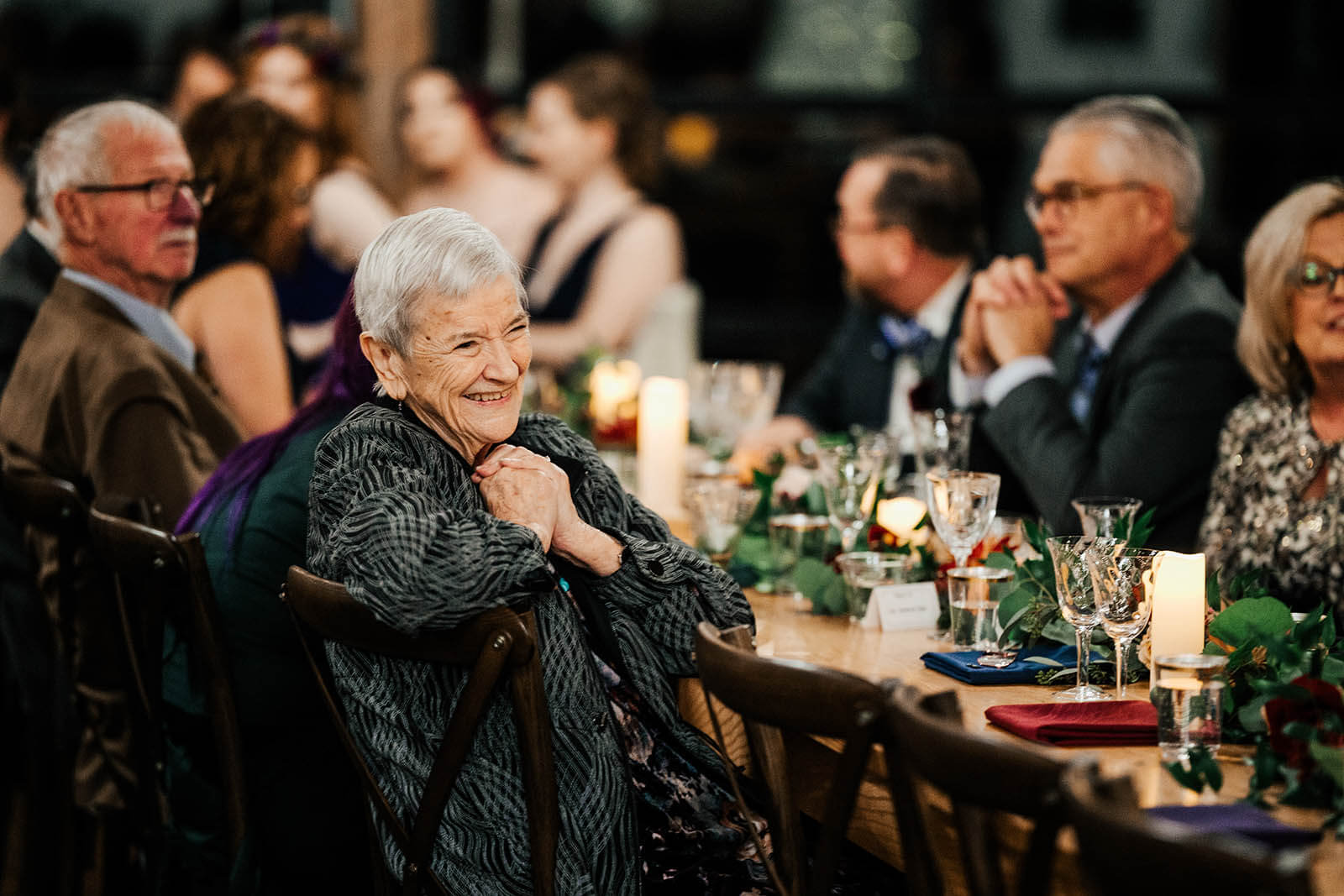 Westers Family Vineyard wedding photographer Jackson Michigan candid grandmother smiling with hands clasped watching wedding reception by candlelight, top Michigan winery documentary wedding photography