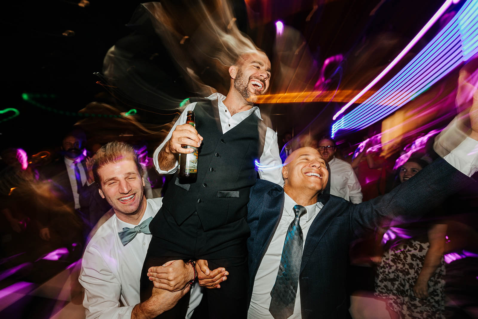 Elevate One Campus Martius wedding photographer downtown Detroit editorial groom lifted by groomsmen on dance floor with motion blur neon lights, best luxury Detroit Michigan wedding photography