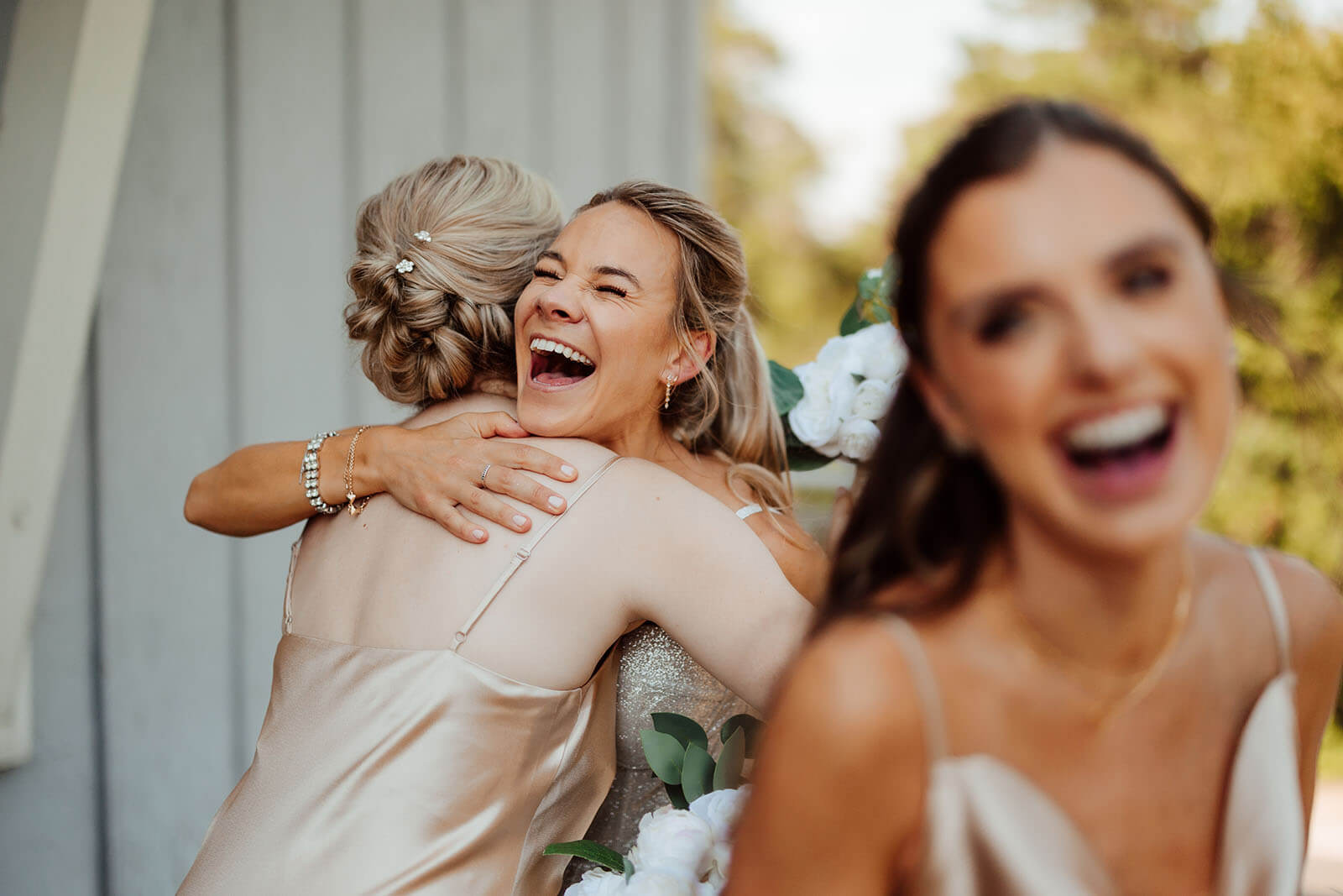 Candid bridesmaids laughing and hugging at Camp Blodgett wedding in West Olive Michigan