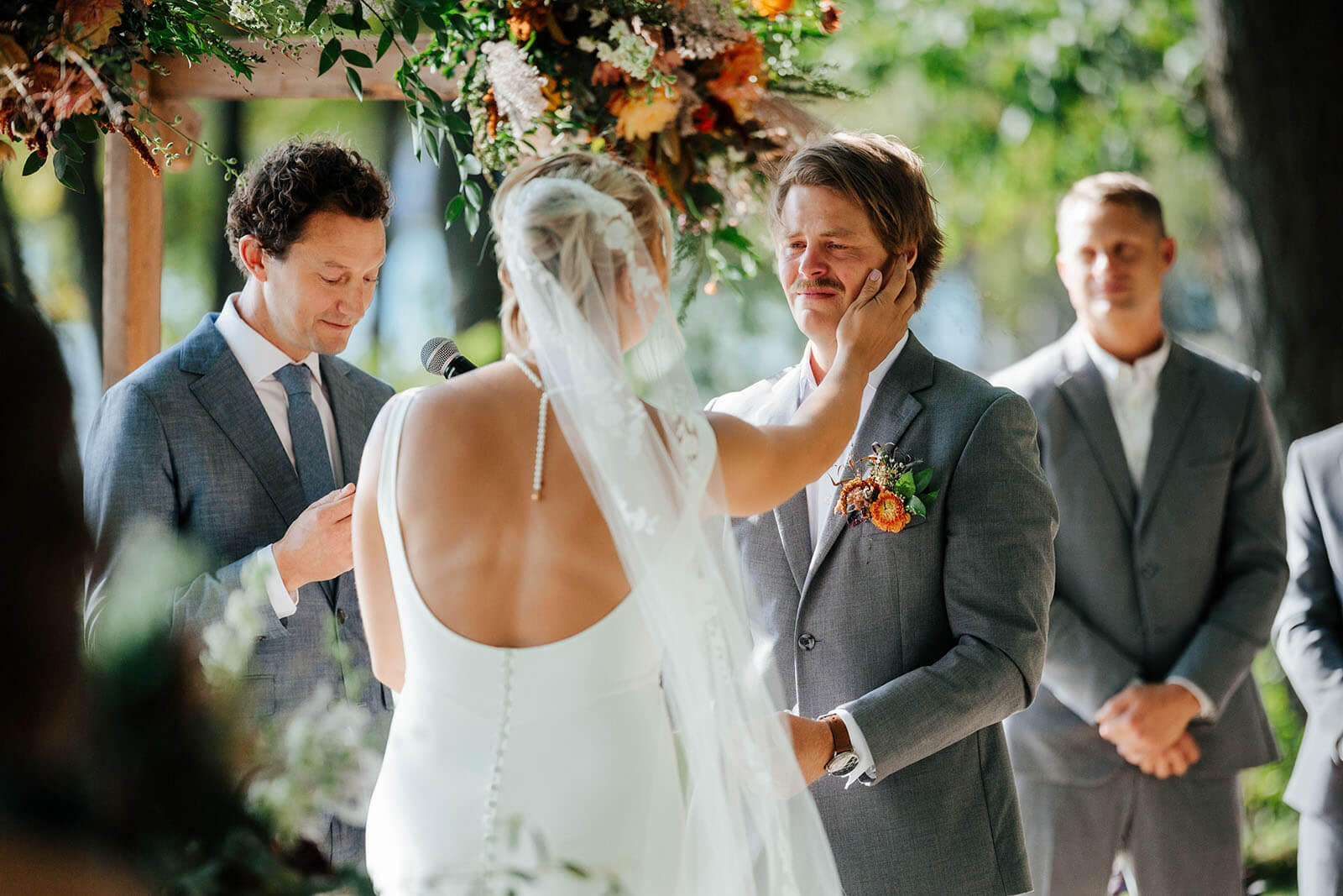 Bride gently wiping groom tears during outdoor ceremony at White Birch Lodge wedding in Elk Rapids Michigan