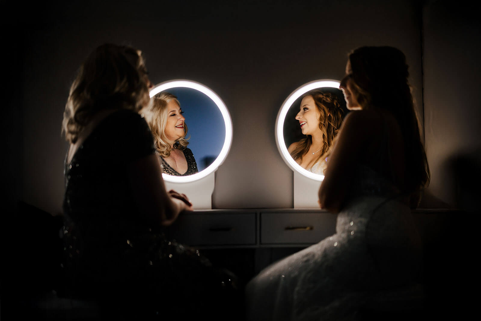 Bride and mother getting ready surrounded by round vanity mirrors at Boatwerks Waterfront wedding in Holland Michigan