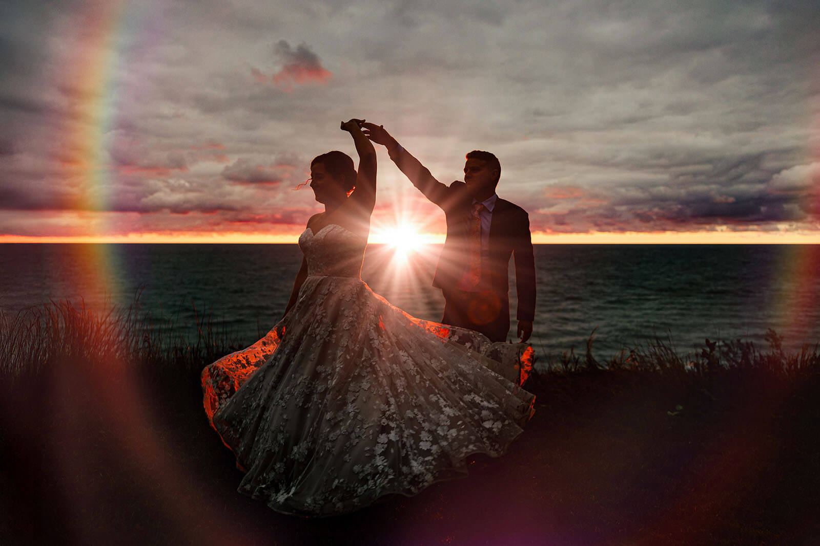 Bride and groom silhouette against Lake Michigan sunset rainbow at backyard wedding in Ludington Michigan