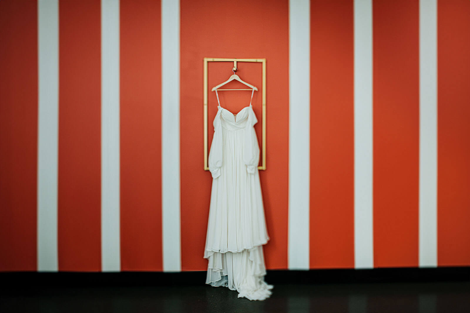 Bride in white gown against gold rack and red striped wall at Leona Road wedding in Grand Rapids Michigan