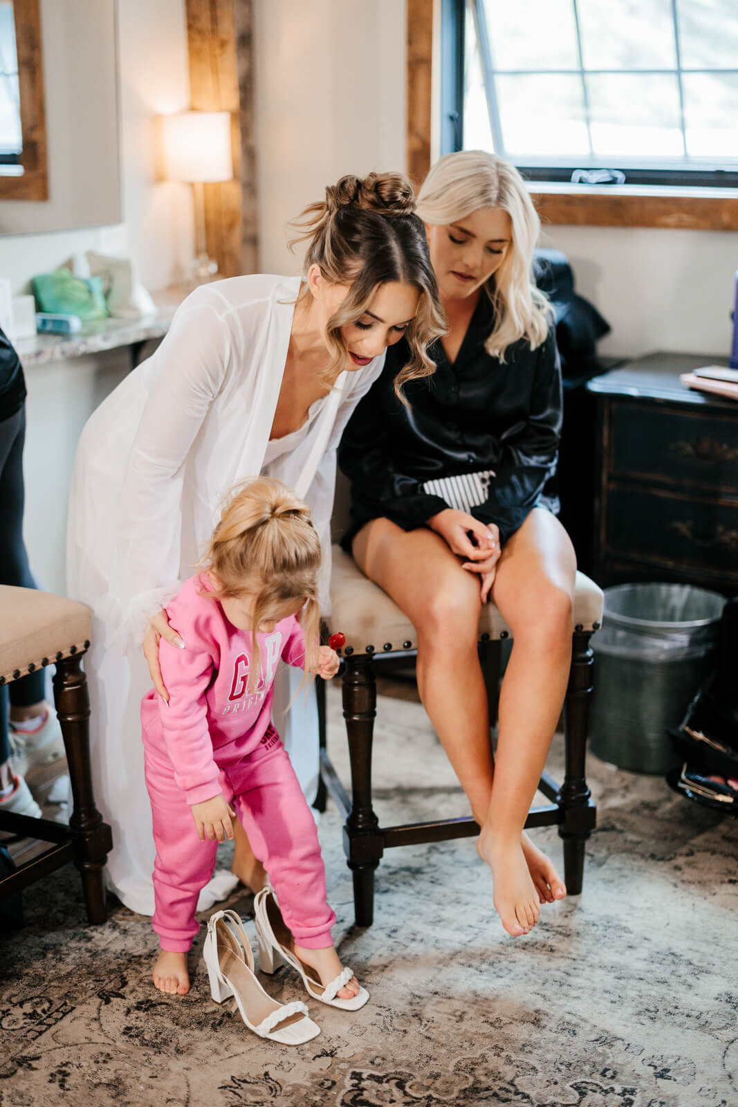 Bride in white robe with flower girl helping put on wedding shoes