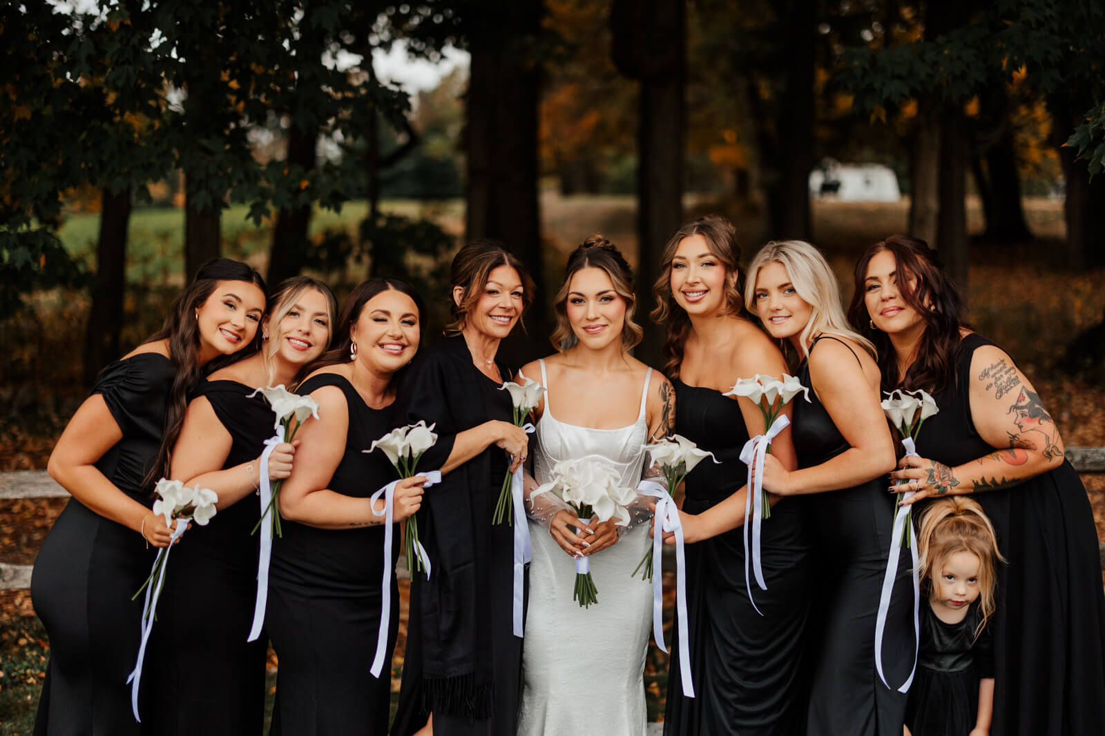 Bridesmaids in black dresses with bride among fall trees at Westers Family Winery