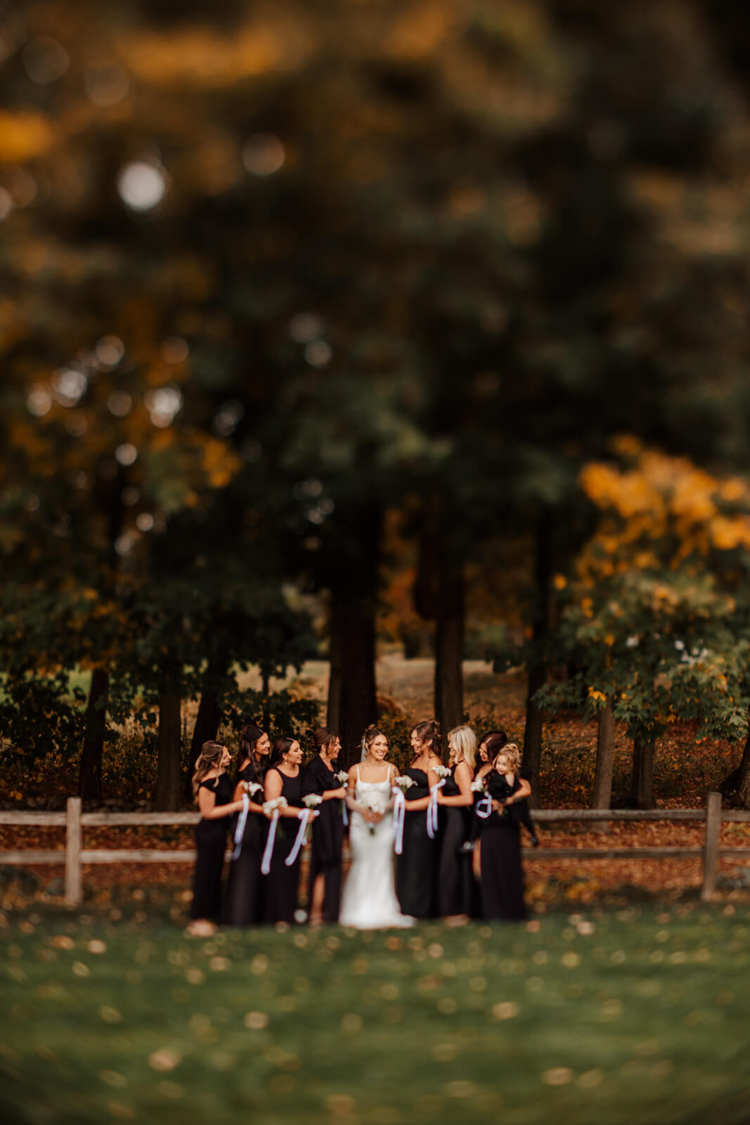 Bridesmaids in black with bride holding calla lilies against fall foliage at winery
