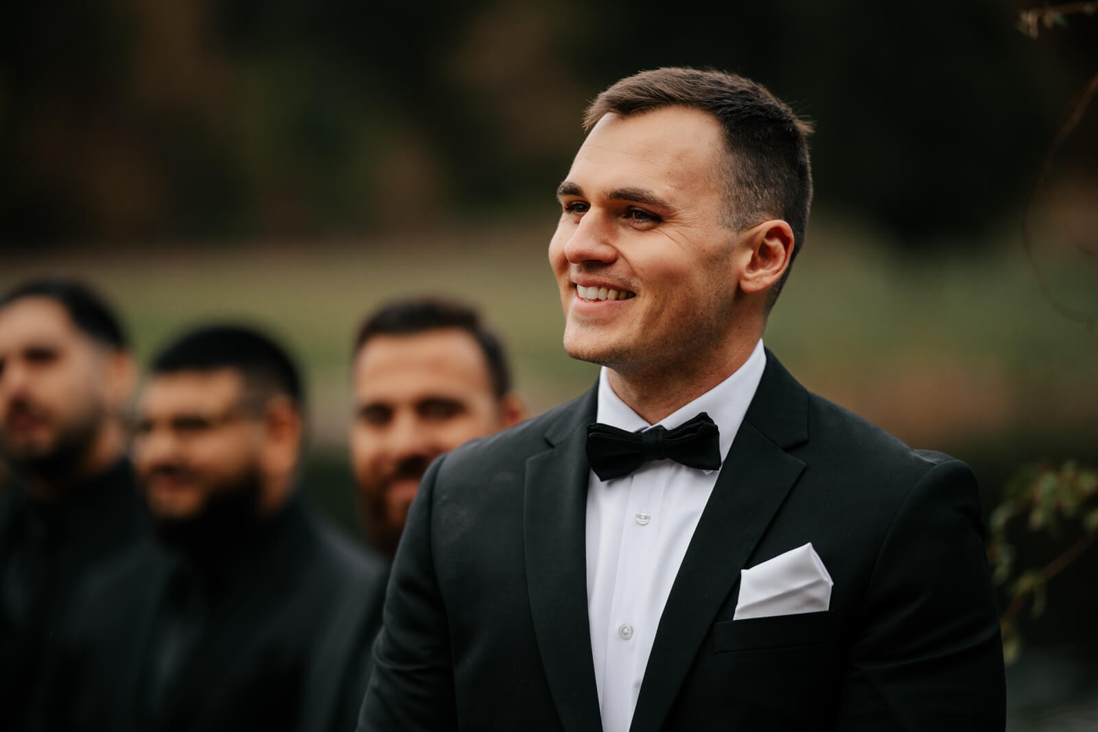 Groom smiling and emotional watching bride walk down aisle at outdoor fall ceremony