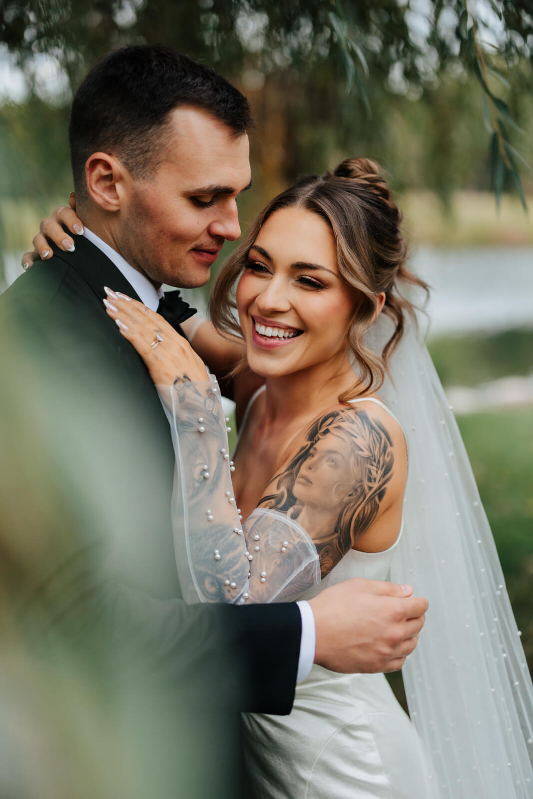 Bride laughing while groom holds her close under weeping willow at fall winery wedding
