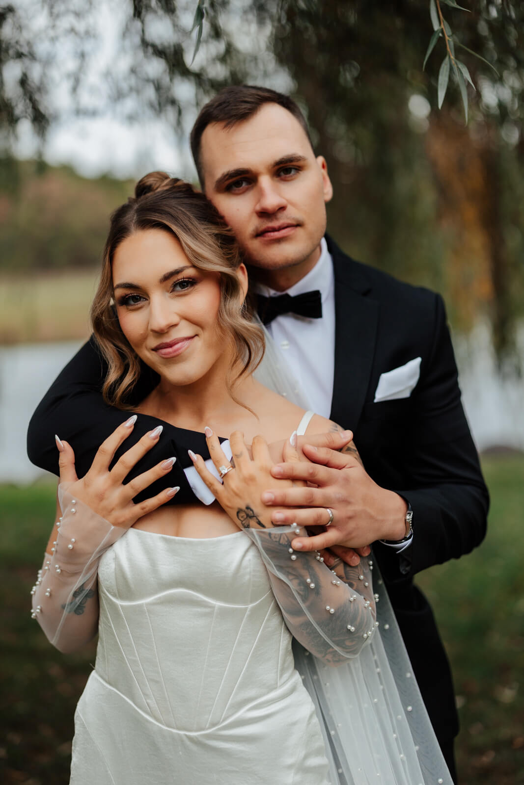 Couple cuddling under weeping willow tattooed bride smiling at camera at Michigan winery wedding