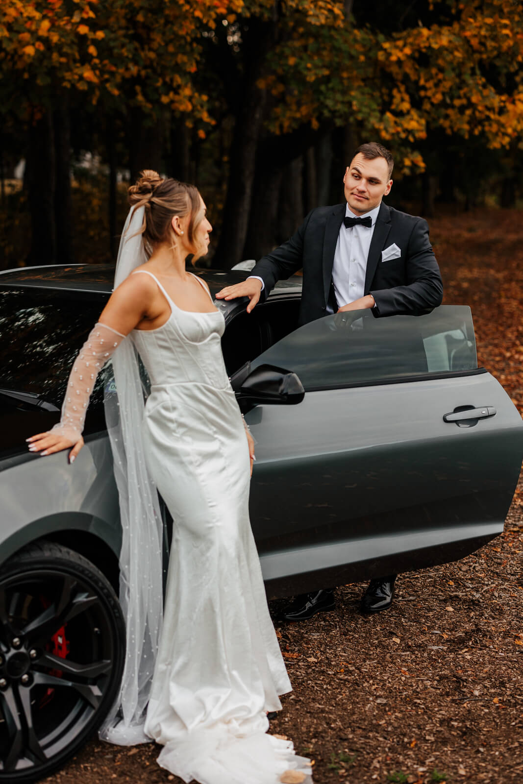 Bride and groom with gray Camaro surrounded by fall foliage at October Michigan wedding