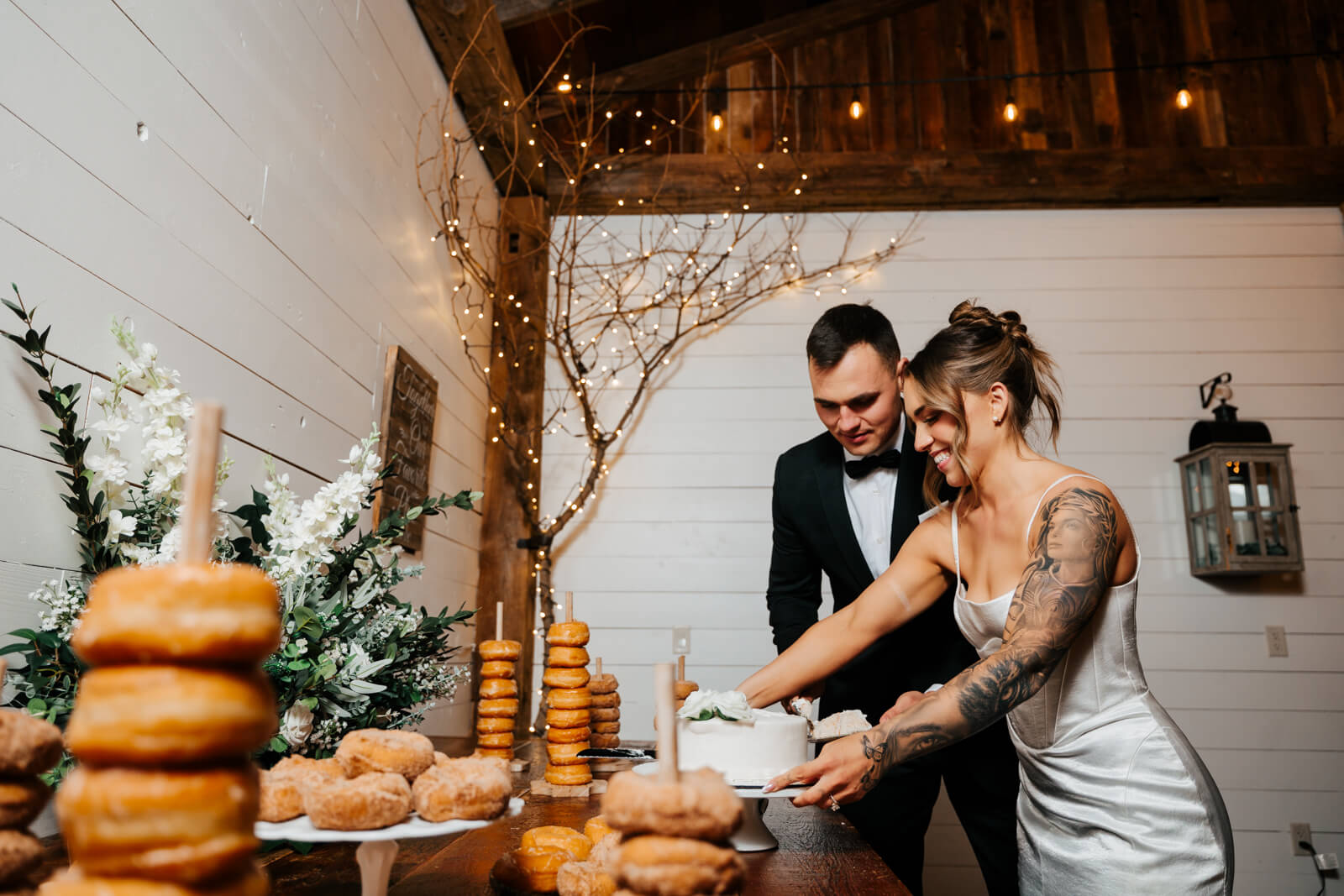 Bride and groom cutting wedding cake beside donut tower at Westers Family Winery reception