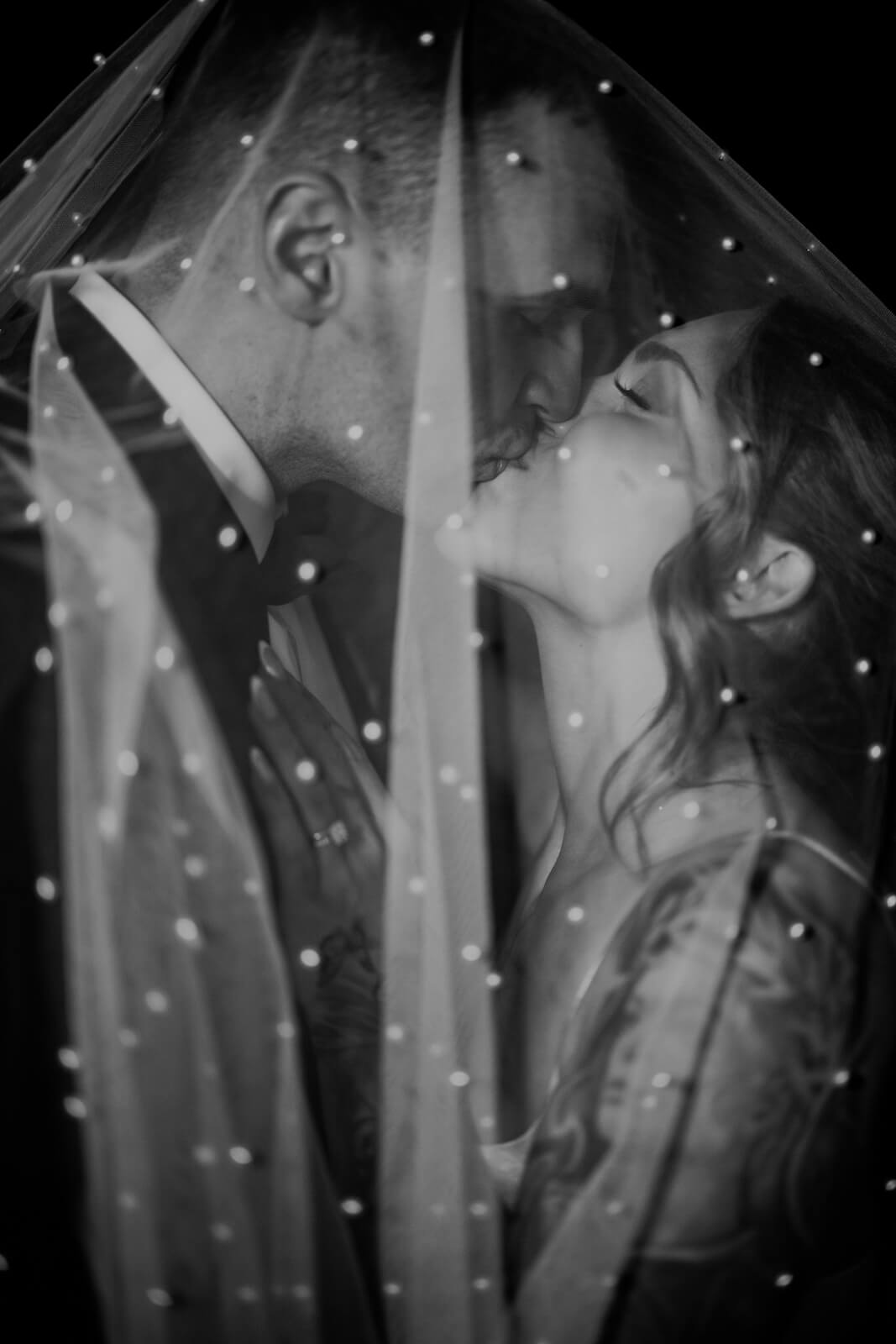 Black and white under-veil portrait of tattooed bride tilting head back at fall winery wedding