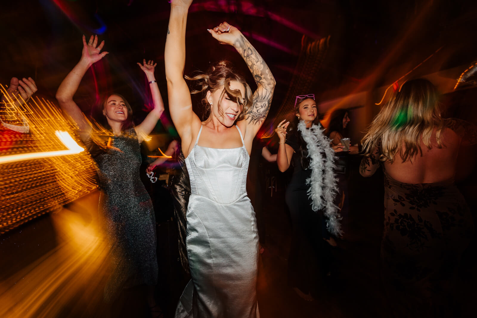 Tattooed bride with arms raised dancing with motion blur light streaks at winery reception