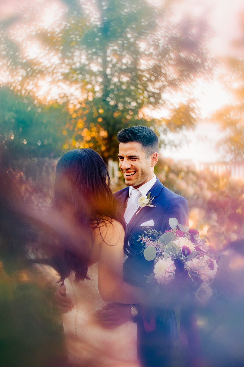 Groom laughing joyfully during golden hour couples portrait with dreamy lens flare