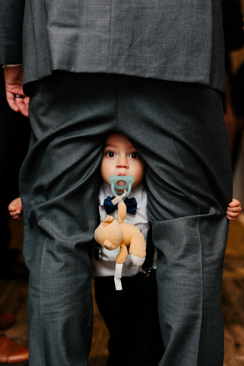 Adorable baby in bow tie peeking through dad's suit jacket holding stuffed animal with pacifier