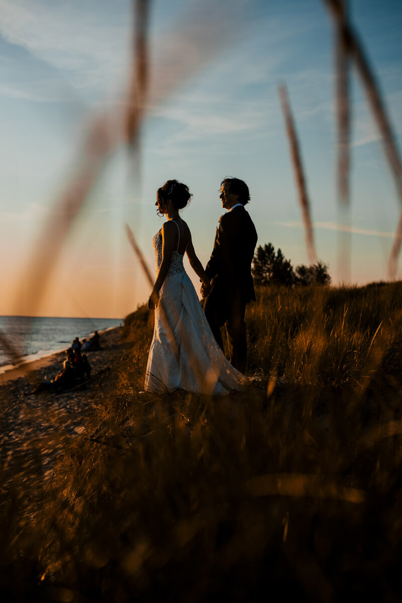 Bride and groom holding hands at Lake Michigan sunset framed by golden dune grass